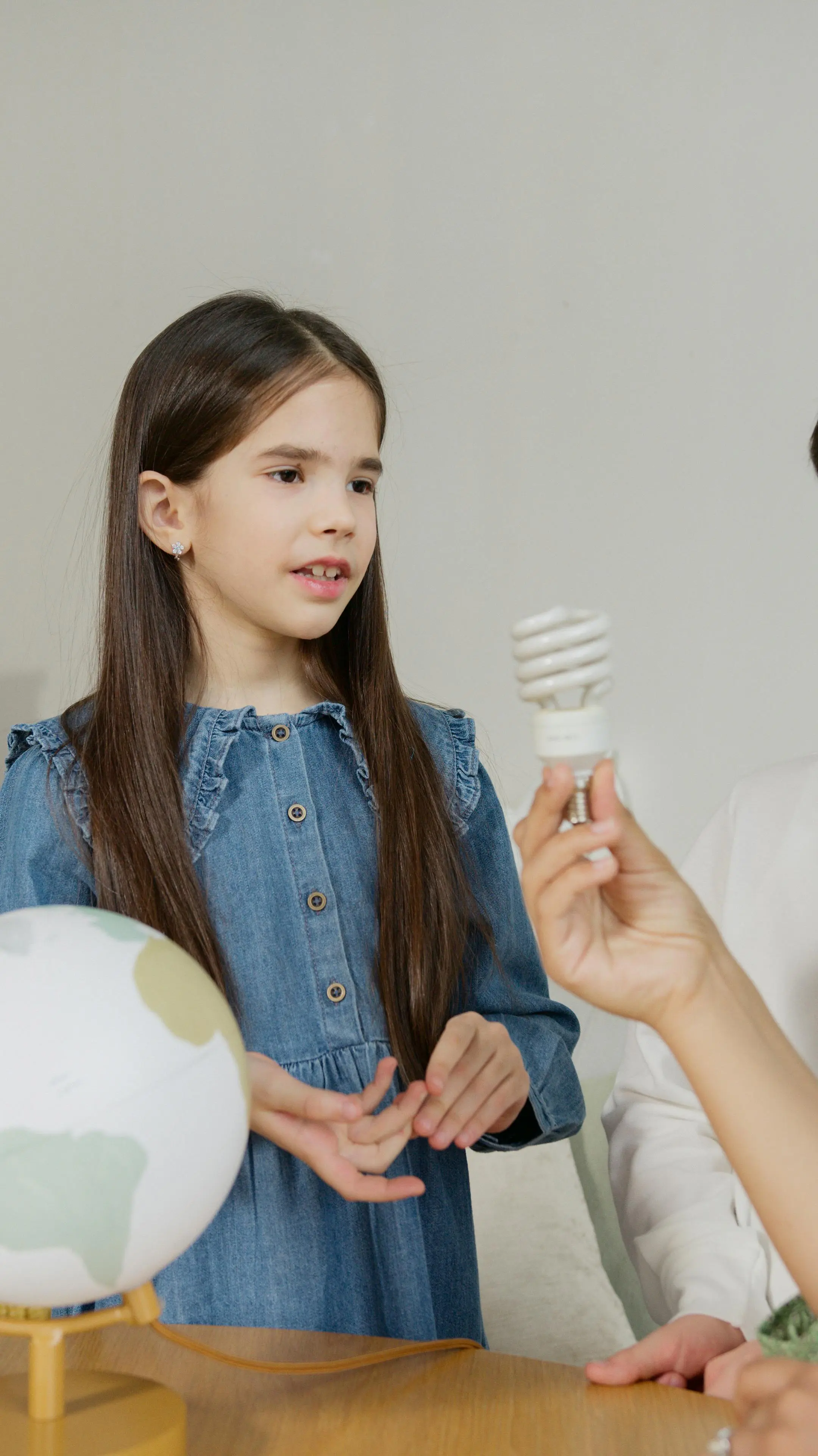 Student examining an energy-saving light bulb beside a globe during a science activity